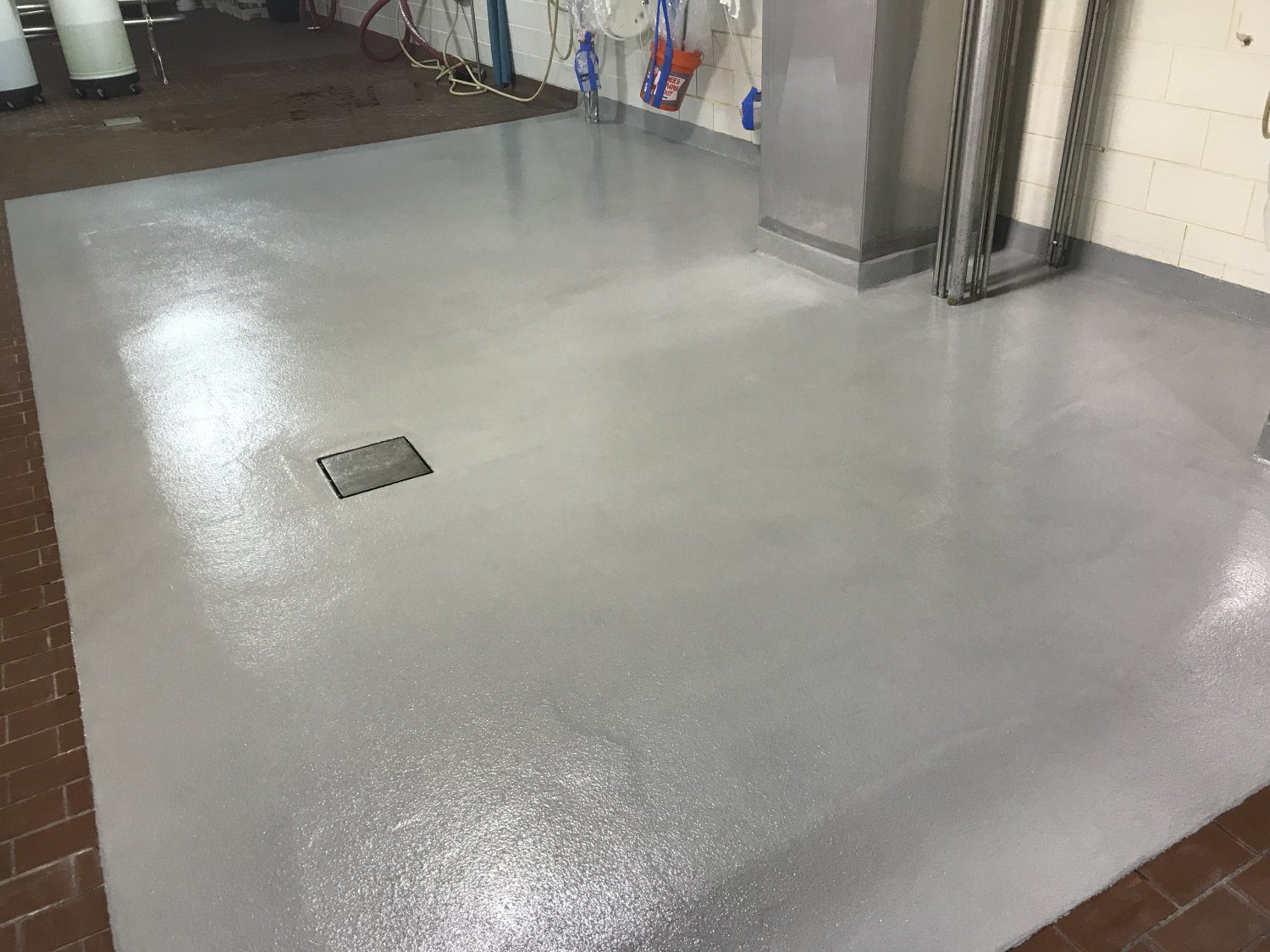 Shiny grey floor with drain and pipes.