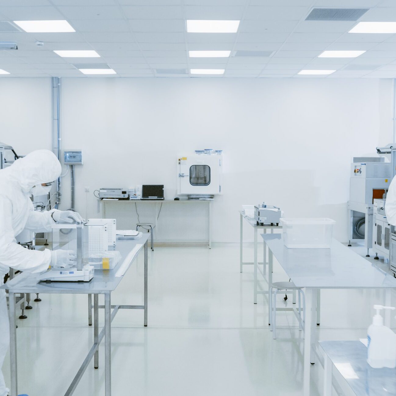 Quality Control Check: Scientist Using Digital Tablet Computer and wearing Protective Suit walks through Manufacturing Laboratory. Product Manufacturing: Pharmaceutics, Semiconductors, Biotechnology.
